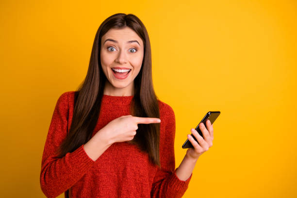 Photo of cheerful attractive overjoyed cute trendy youngster pointing at her telephone expressing amazement with face wearing red sweater isolated over vivid color background Photo of cheerful attractive overjoyed cute trendy youngster pointing at her telephone expressing amazement with face wearing, red sweater isolated over vivid color background aiming photos stock pictures, royalty-free photos & images