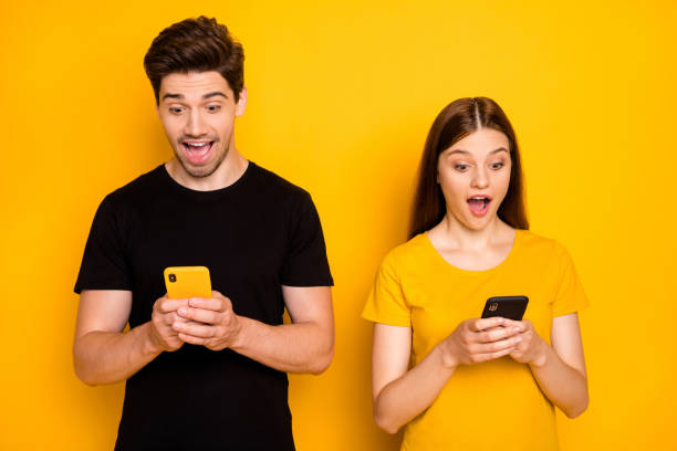 photo of cheerful excited crazy ecstatic overjoyed about receiving messages from each other girlfriend and boyfriend stylish trendy isolated in black t-shirt over vivid color yellow background - friends color background imagens e fotografias de stock