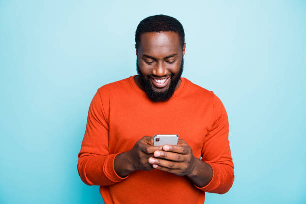 foto van vrolijke positieve knappe mens die telefoon houdt die toothily het zoeken informatie nieuwe geïsoleerde levendige blauwe kleurenachtergrond glimlacht - gekleurde achtergrond stockfoto's en -beelden