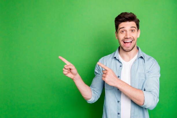 photo of cheerful positive handsome man pointing at empty space expressing ecstatic emotions on face with bristle isolated over green vivid color background - man pointing imagens e fotografias de stock
