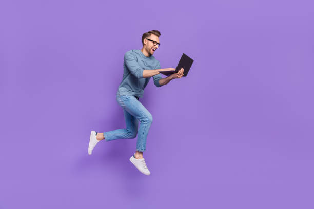 Photo of excited bust guy wear grey shirt spectacles jumping high typing modern device isolated violet color background stock photo