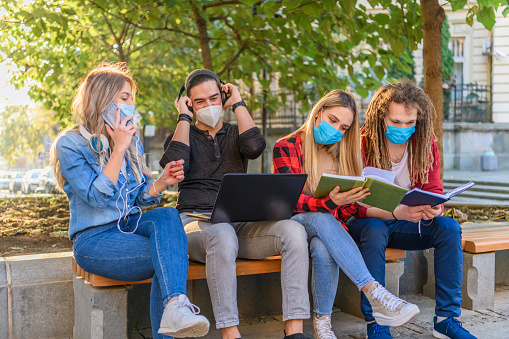 Confident Students are Avoiding Crowded Places due to Virus Outbreak so they are Sitting in the Park and Working from Distance on a Laptop While Wearing Face Masks.