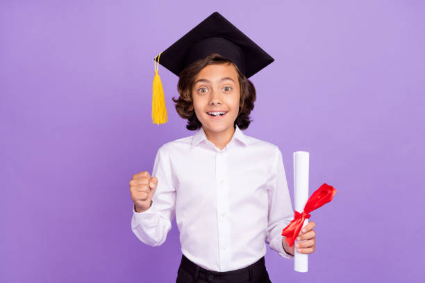 Photo of funny small brunet boy hold paper wear formalwear cap isolated on purple color background stock photo