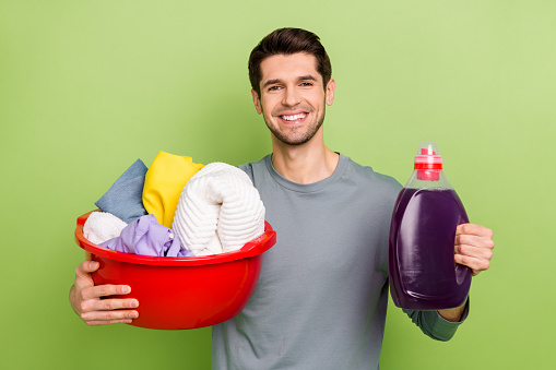 Photo of millennial optimistic brunet guy do laundry hold bottle wear shirt isolated on green color background.