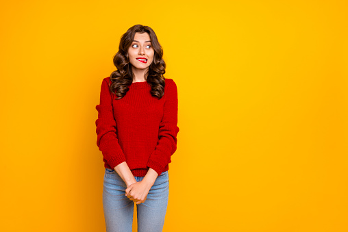 Photo of pretty curly wavy charming cute cheerful nice good girlfriend, standing hesitating and shy looking away at something with hands folded isolated over yellow vivid color background