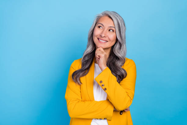 Photo of shiny dreamy senior lady dressed yellow blazer arm chin looking empty space smiling isolated blue color background stock photo
