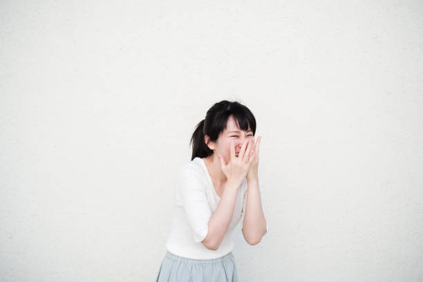 Photo of smiling Asian woman in front of white wall Photo of smiling Asian woman in front of white wall. shy japanese woman stock pictures, royalty-free photos & images