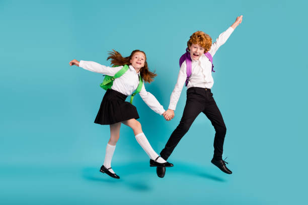 Photo of two crazy schoolchildren hold hands jump wear white shirt uniform isolated blue color background stock photo