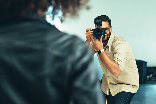 Photographer focusing his DSLR camera on a model during a photo shoot. Photographer taking photos connecting his camera to a laptop.