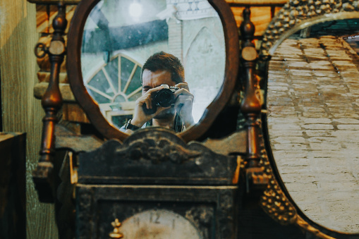 Photographer shooting his camera in front of a mirror in an antique store. Man taking a self-portrait with his professional camera.