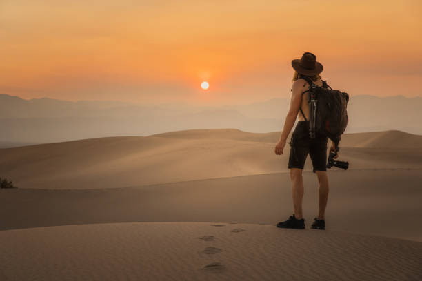 Photographer standing in desert sand dunes at sunset stock photo