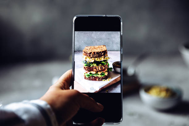 Photographing large vegan sandwich with smartphone Woman using a mobile phone to take photograph of a large vegan sandwich. Woman's hand taking pictures of super sandwich on the table with his smartphone. sandwich photos stock pictures, royalty-free photos & images