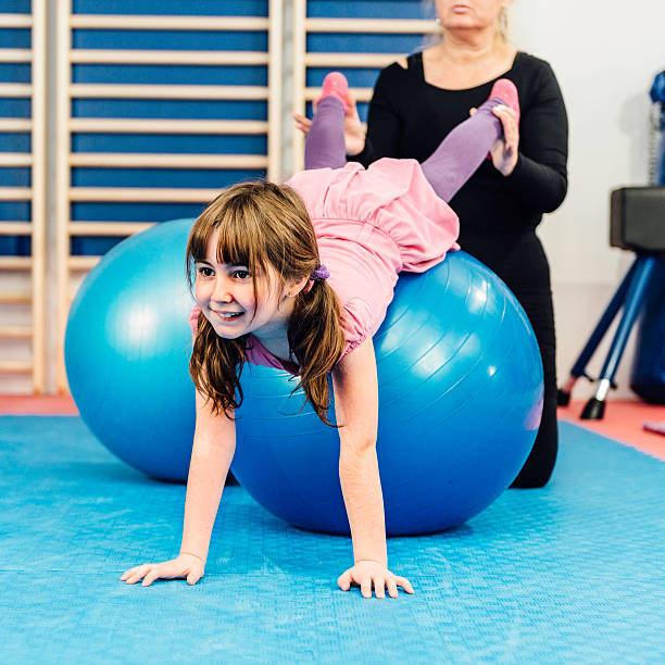 Physical therapist working with little girl Physical therapist working with little girl in gym, exercising with fitness ball yoga ball work stock pictures, royalty-free photos & images