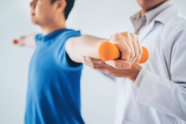 Physiotherapist man giving exercise with dumbbell treatment About Arm and Shoulder of athlete male patient Physical therapy concept stock photo