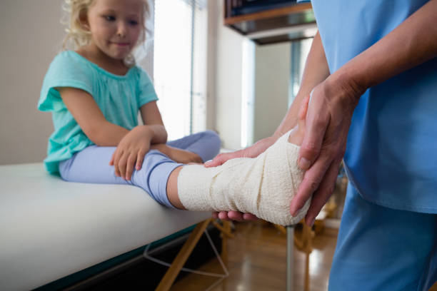 Physiotherapist putting bandage on injured feet of girl patient Physiotherapist putting bandage on injured feet of girl patient in clinic orthopedics stock pictures, royalty-free photos & images