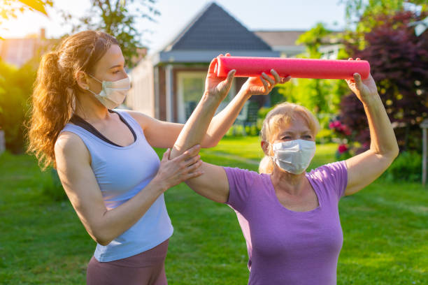 Physiotherapist working with elderly patient outdoors both wearing medical masks Sport exercises at nursing home with assistant, using coronavirus protection measures after or during quarantine drug rehab stock pictures, royalty-free photos & images