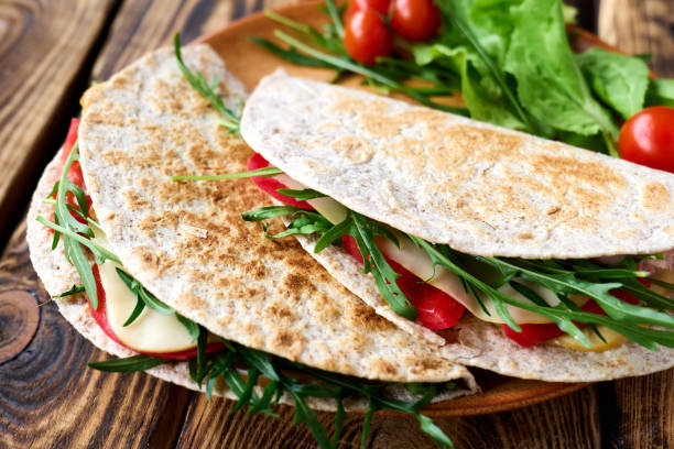 Piadina Romagnola with mozzarella cheese, tomatoes, ham and rocket salad on wooden table. Italian flatbread or open sandwich. Selective focus. Piadina Romagnola with mozzarella cheese, tomatoes, ham and rocket salad on wooden table. Italian flatbread or open sandwich. Selective focus. emilia romagna stock pictures, royalty-free photos & images