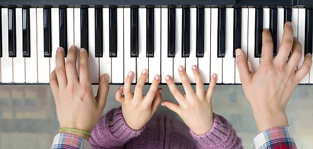 Piano Keyboard top View and Hands of Child and Mother stock photo