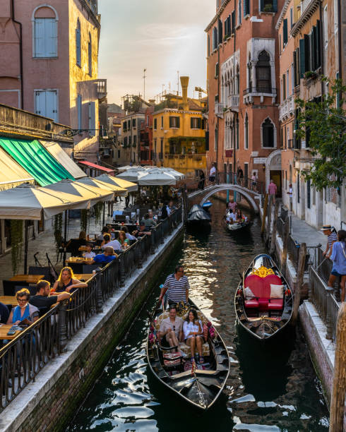 Picturesque Venice canal with gondolas and tourists on the right enjoying the sunset in a cocktail bar stock photo