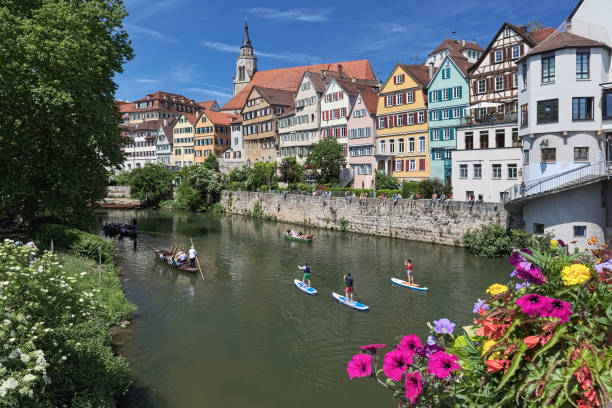 Picturesque view of the historical houses at the riverside of Neckar in Tubingen, Germany Tubingen, Germany - May 21, 2018: Picturesque view of the row of historical houses across the riverside of Neckar in the university town of Tubingen in central Baden-Wurttemberg. Unknown people ride along the river on the traditional punt boats and standup paddle boards, and have a rest at the embankment. View from bridge which always decorated in warm season with multicolored natural flowers. baden baden stock pictures, royalty-free photos & images
