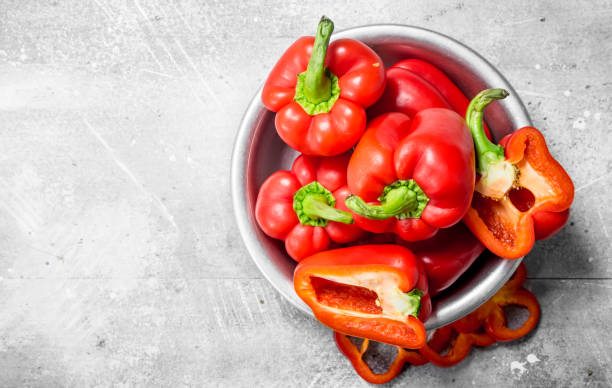 Pieces of sweet pepper and whole red peppers in the bowl. stock photo