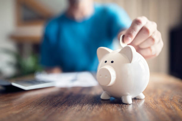 Piggy bank savings Man putting a coin into a pink piggy bank concept for savings and finance savings stock pictures, royalty-free photos & images