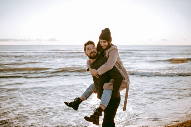 Piggyback couple at the beach celebrating their honeymoon at the winter time. stock photo
