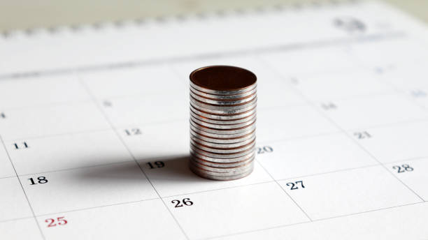A pile of coins on the calendar. A pile of coins on the calendar. monthly event stock pictures, royalty-free photos & images