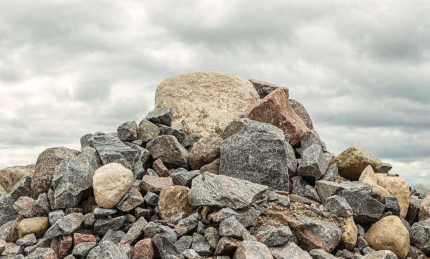 pile of huge rocks and boulders under dark grey sky horizontal image of big pile of rocks and boulders piled high under a grey cloudy rainy day in summer time with room for text. boulder rock stock pictures, royalty-free photos & images