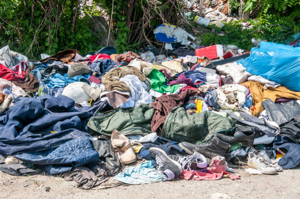 Pile of old clothes and shoes dumped on the grass as junk and garbage, littering and polluting the environment stock photo