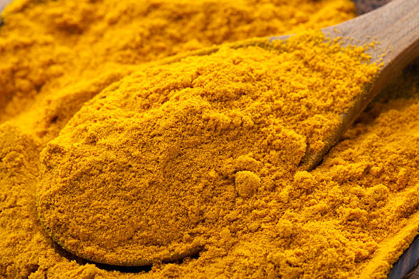 A pile of turmeric in a bowl with a wooden spoon stock photo