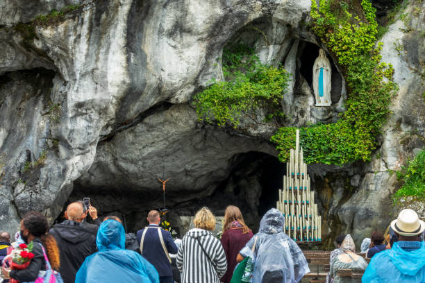 Pilgrims praying the statue of Virgin Mary in the grotto of Our Lady of Lourdes, France stock photo