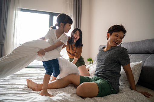 An Asian family and their daughter are having a pillow fight time in the bed.