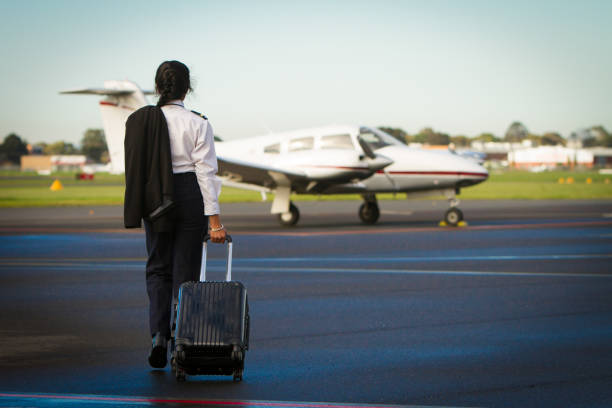 Pilot Departing A female pilot walks towards her aircraft. She has her uniform on, jacket over the shoulder, and is pulling a suitcase. pilot stock pictures, royalty-free photos & images