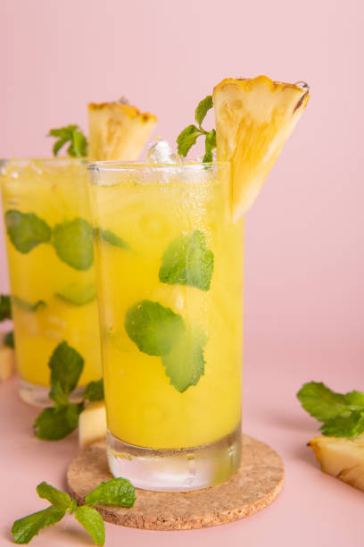 Pineapple cocktail or fresh pineapple juice, mint leaves in glass with ice and  pineapples on a pink background. selective focus. stock photo