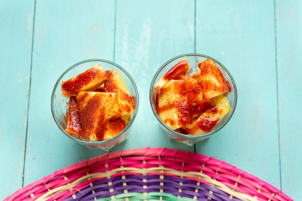 piña cortada con chile en polvo y salsa picante en vidrio sobre fondo turquesa - fruta con chamoy fotografías e imágenes de stock