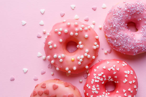 Pink donuts with icing and sugar sprinkles on a pastel pink background top view. stock photo