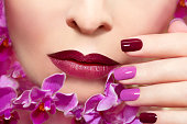 Pink maroon manicure on a young woman with orchids.