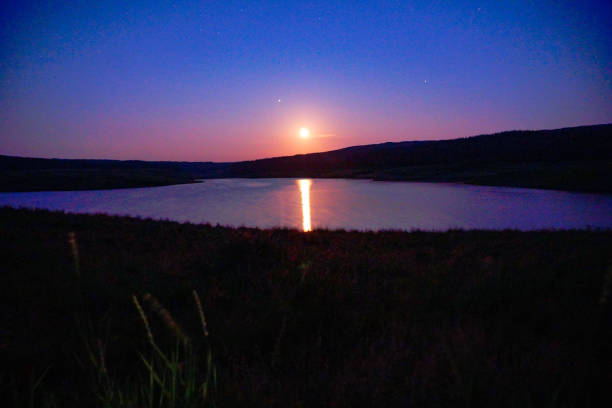 pink moonset reflection on lake in long exposure stock photo