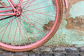 Color image depicting a pedal bicycle painted a vibrant shade of pink. The bike is leaning against an aqua blue wall that is weathered and ruined - the paint is peeling off. The bright color of the bike contrasts nicely with the hue of the wall. The bicycle is decorated with a couple of flowers. Lots of room for copy space.