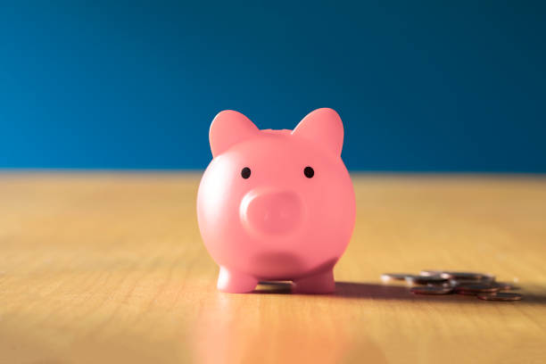 pink piggy bank on wooden office desk at home with pile of coins, savings,investment business and financial concept - pensioen nederland stockfoto's en -beelden