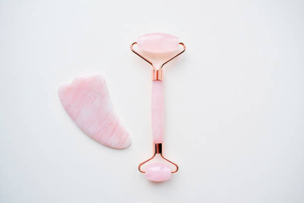 Pink roller face massager and gouache scraper . Rose quartz jade roller on a white background. Anti age, lifting and toning treatment at home. Copy space. Pink roller face massager and gouache scraper . Rose quartz jade roller on a white background. Anti age, lifting and toning treatment at home. Copy space. rose quartz stock pictures, royalty-free photos & images