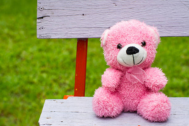 smiling pink teddy bear looks very happy sitting on a vintage bench,...