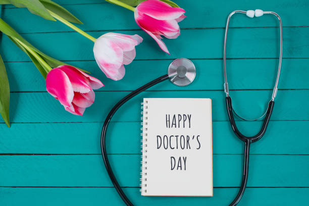 Pink tulips and stethoscope with spiral notepad with Happy Doctors Day text on it. stock photo