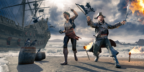 Male and female pirate walking on a beach near a pirate ship and barrels, near the shore under a stormy sky. The pirates are wearing historical pirate costumes, and holding up a sword, cutlass and torn pirate flag. There are flaming torches stuck into the sand and flames nearby.