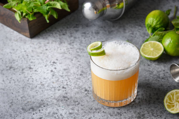 Pisco sour cocktail - whiskey with lime juice, sugar syrup and egg white. Close up. Pisco sour cocktail - whiskey with lime, egg white, sugar syrup in glass on grey table. Space for text. sour taste stock pictures, royalty-free photos & images