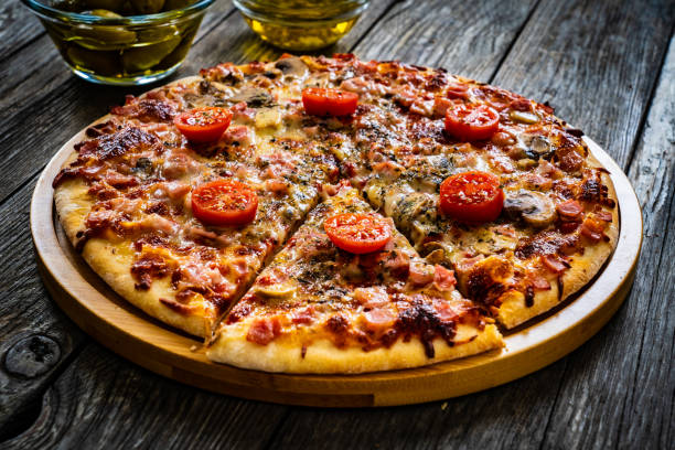 Pizza capricciosa with white mushrooms, ham, tomatoes and mozzarella on wooden background stock photo