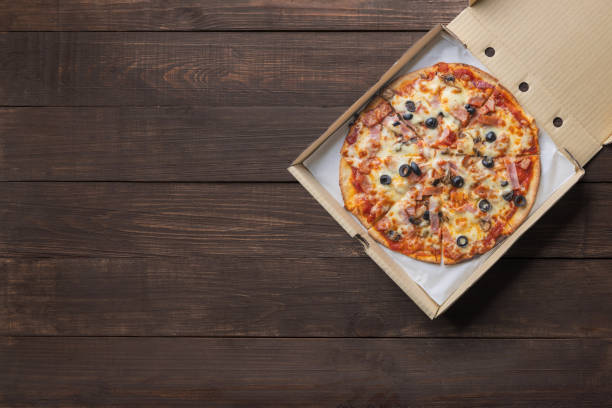 pizza in paper box on wooden background. copyspace for text and logo. top view. - pizza table imagens e fotografias de stock