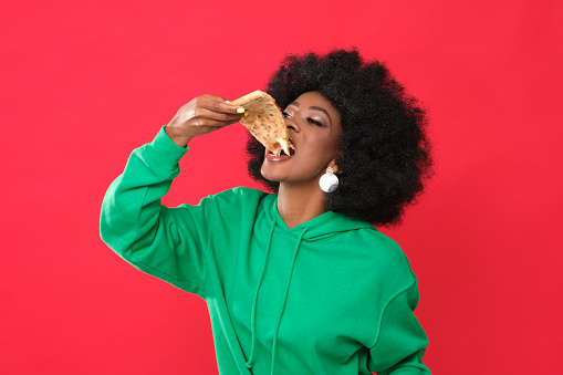 Food lover. Afro girl eating pizza. Studio shoot.