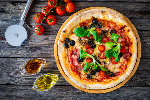 Pizza prosciutto with white mushrooms, tomatoes and mozzarella on wooden background stock photo